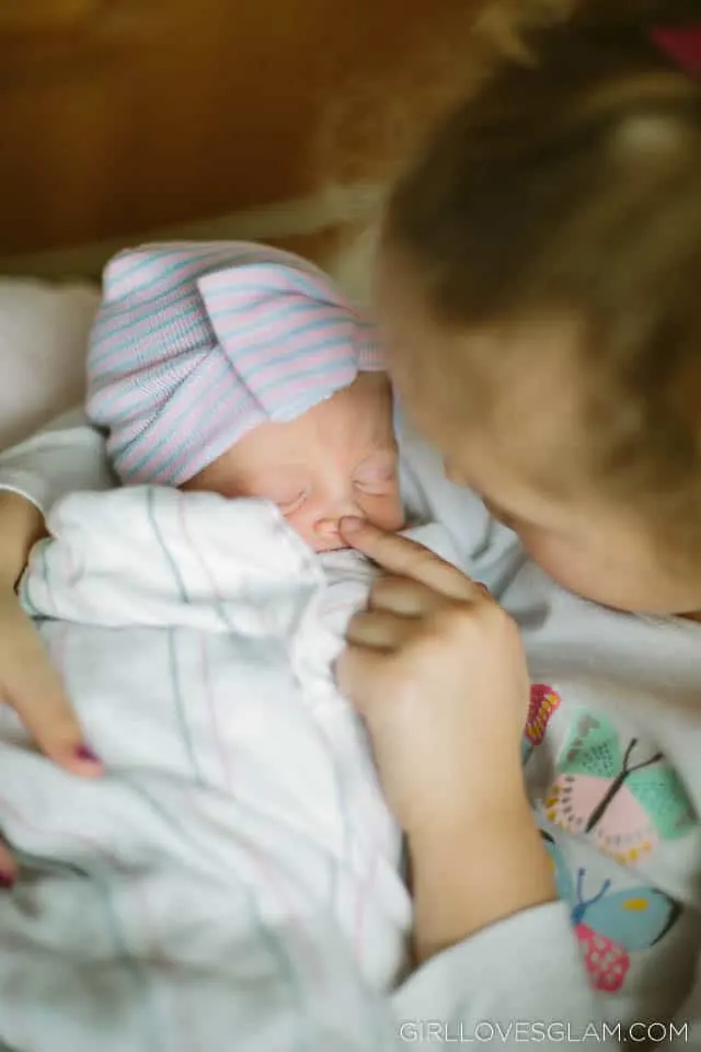 Big sister holding baby sister at the hospital on www.girllovesglam.com